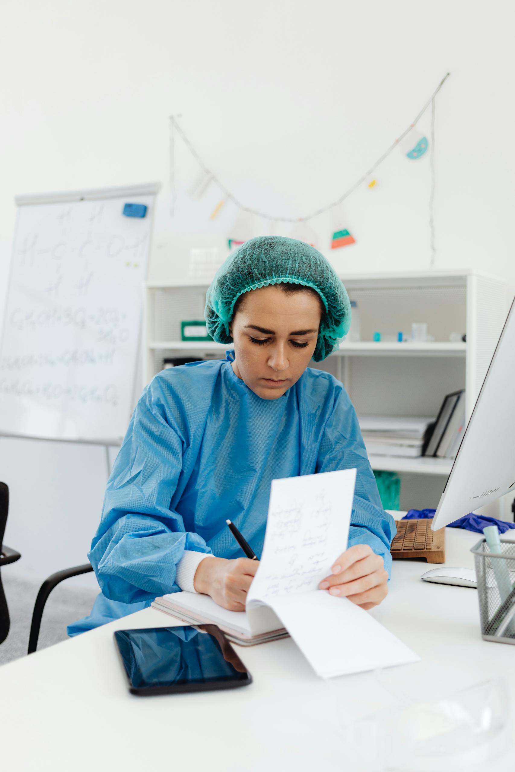 Female doctor in scrub suit writing notes in a hospital laboratory environment.